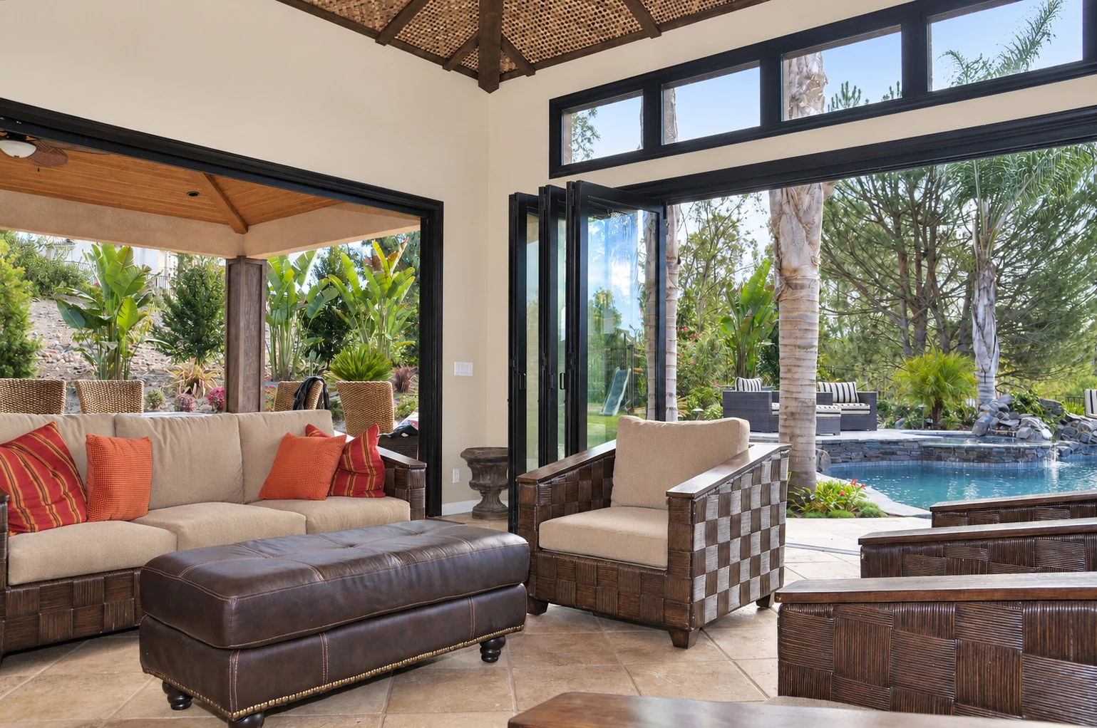 Open dark framed bifold doors connecting a furnished living area with a garden and pool