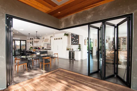 Open zero-post corner doors connecting a wood deck to the kitchen and dining room.