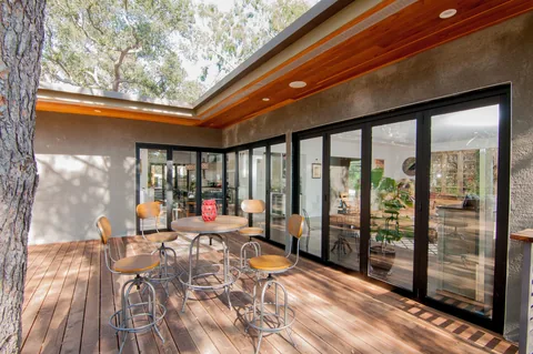 Exterior deck with a dining table beside closed aluminum corner doors.