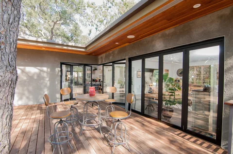 Outdoor dining deck facing the glass walls of a residential corner-door system.