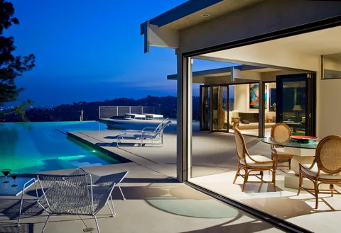 A pool terrace beside open corner folding doors at dusk.