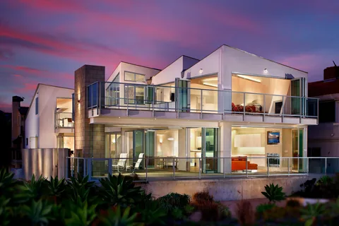 A two-story home with expansive glass openings at dusk.